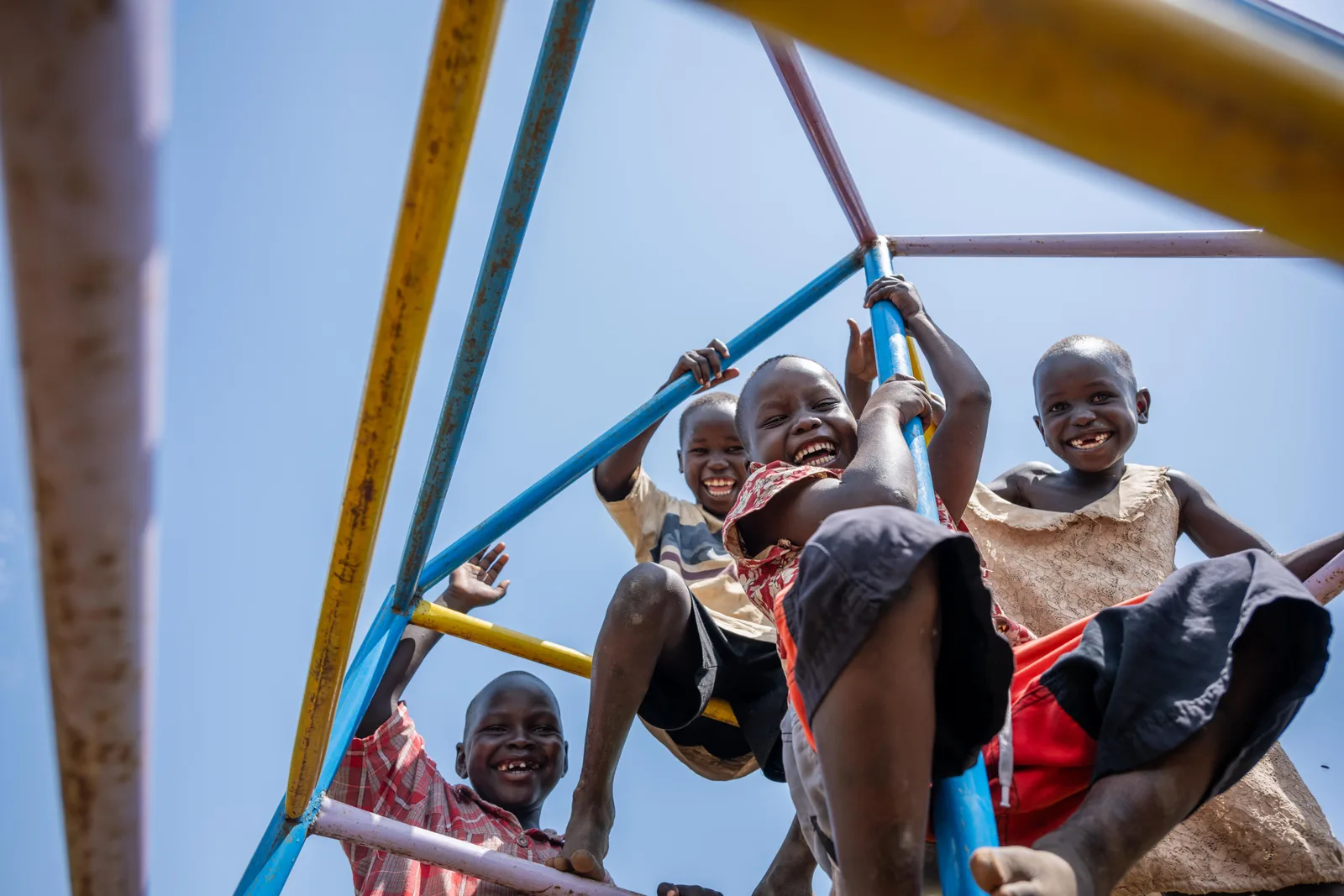 Children playing on a climbing frame, seen from below against the sky.