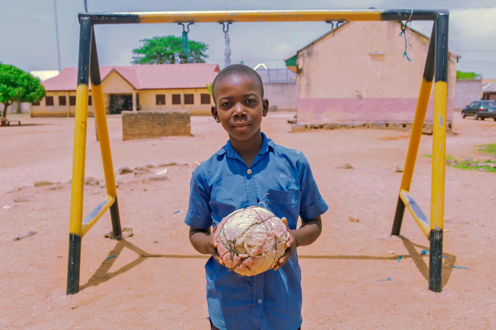 A boy stands holding a football beside a swing in a school yard.