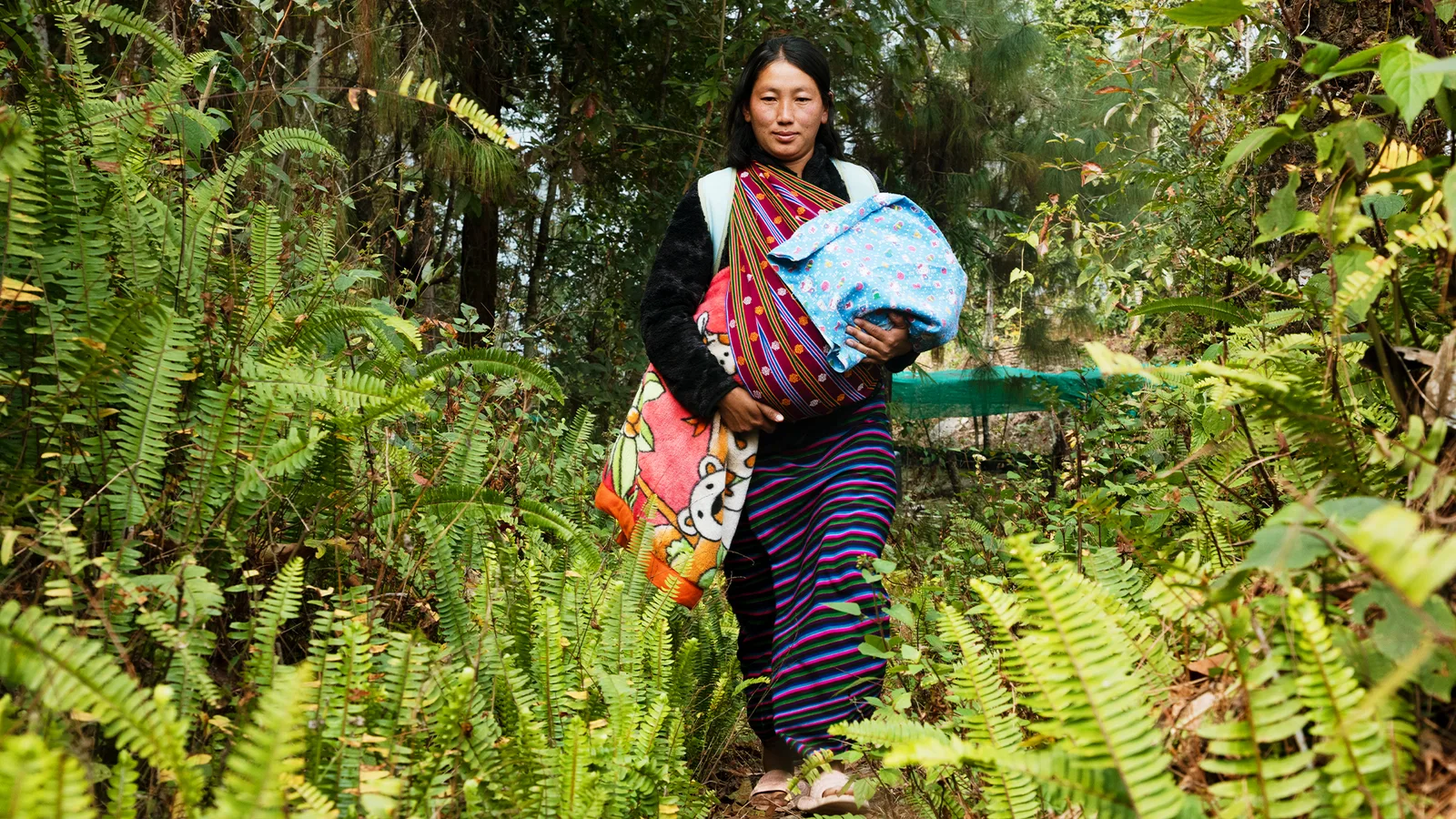 A woman carries her baby along a path through dense green vegetation.