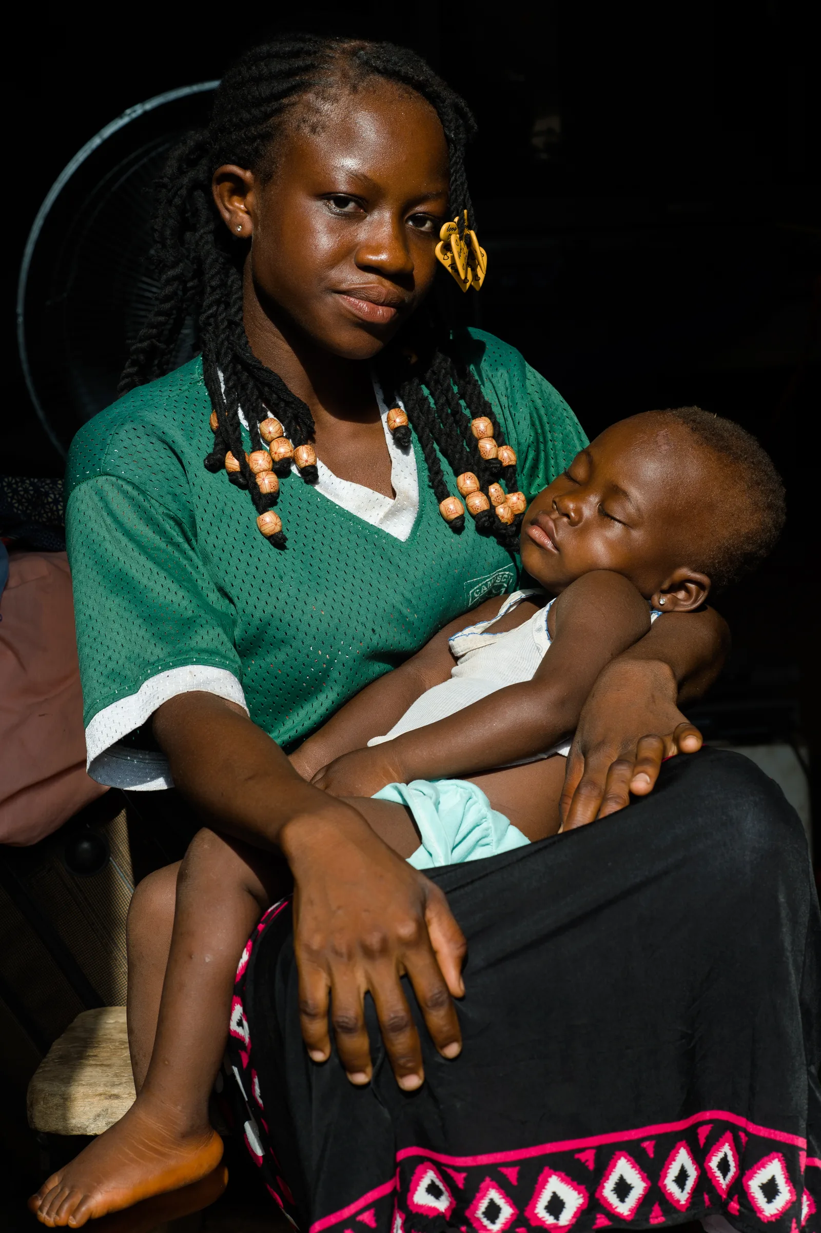 A young woman holds a sleeping child in her arms.