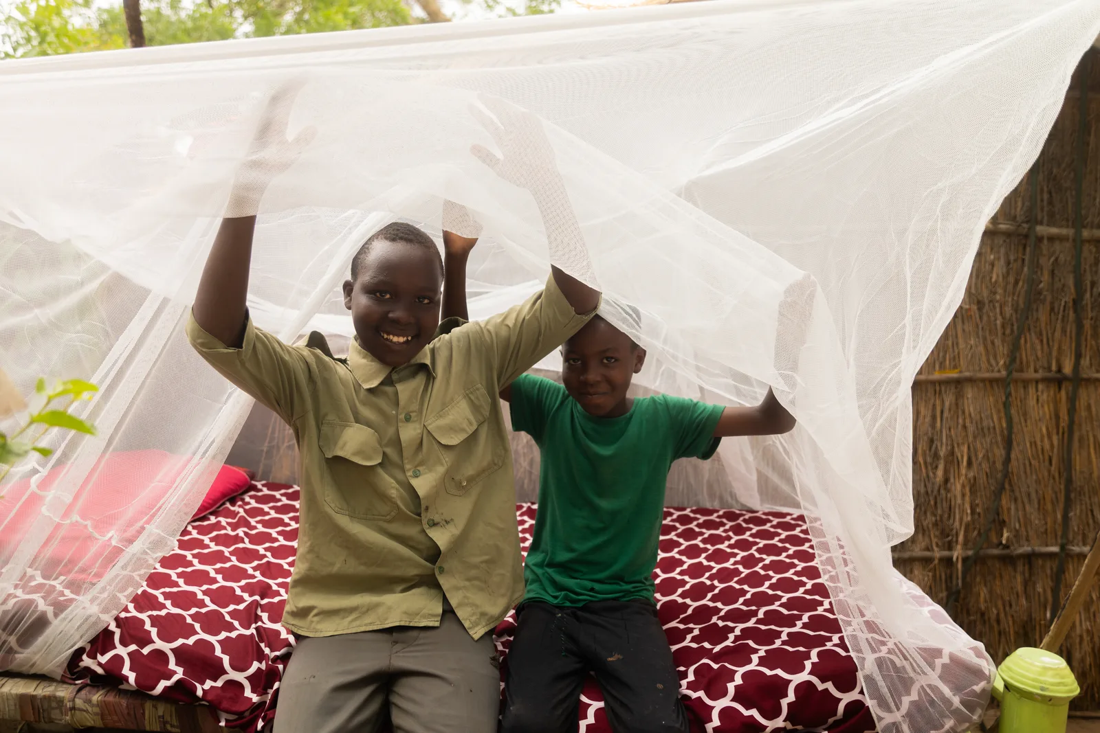 Two boys smile as they hang an insecticide-treated mosquito net over a bed.