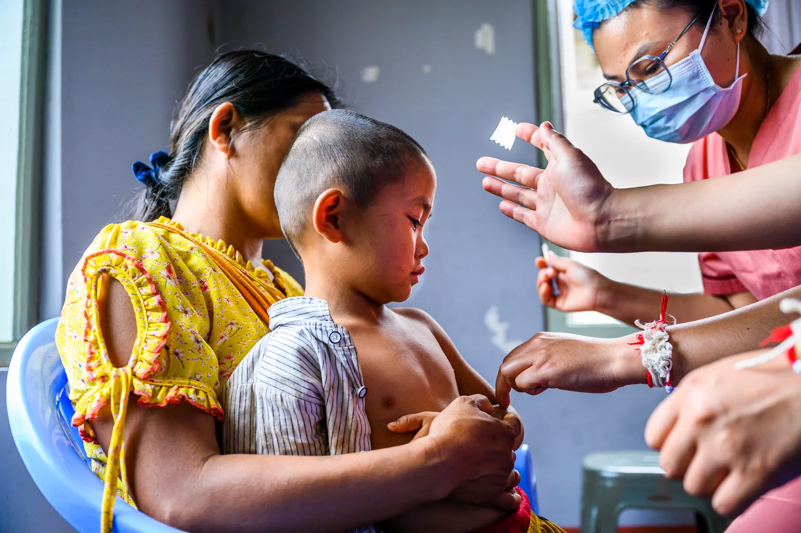 A health worker attends to a young child held by their mother at a clinic.