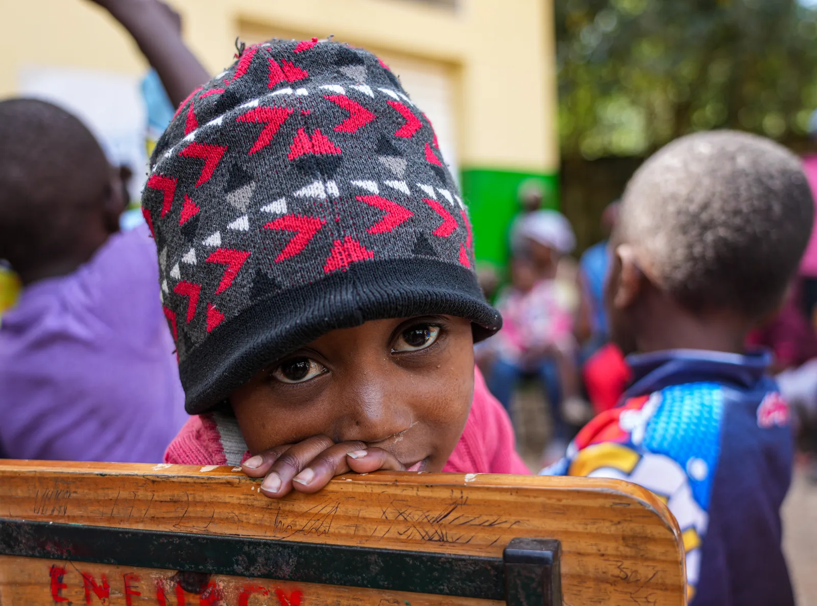 A child in a knitted hat resting their chin on a school desk.