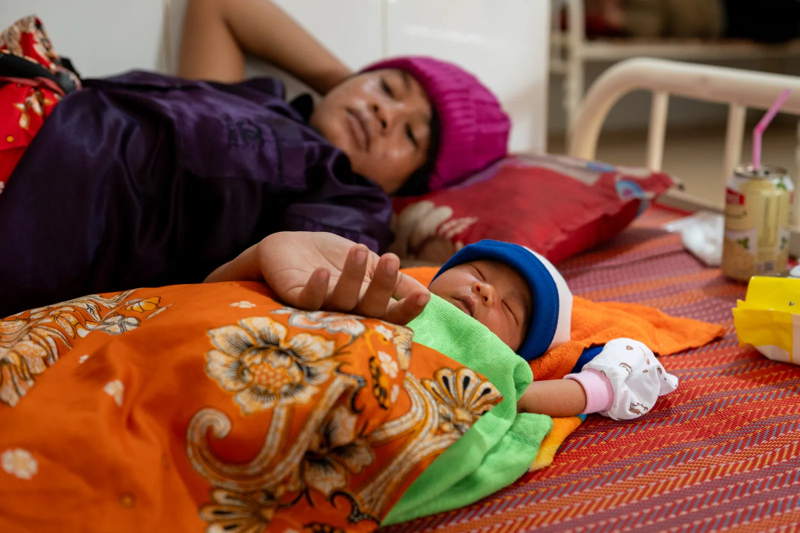 A mother rests on a bed with her newborn lying next to her.